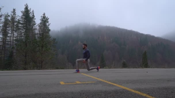 天然の背景に足のためのストレッチ演習を行う運動体を持つハンサムな強い男 — ストック動画