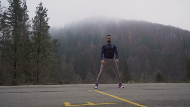 Vista frontal del hombre fuerte y saludable. Chico estirando los músculos antes de correr al aire libre en un día brumoso — Vídeos de Stock