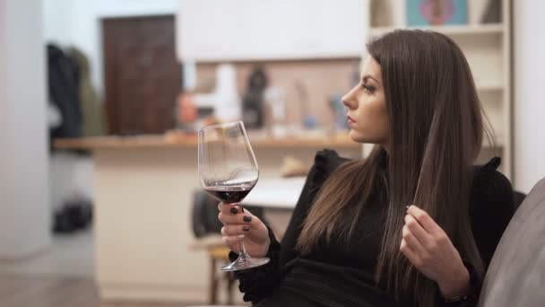 Hermosa mujer en vestido negro sosteniendo copa de vino y jugando con su pelo largo — Vídeos de Stock