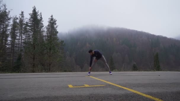 Hombre fuerte y flexible estirándose antes de la sesión de entrenamiento al aire libre en las montañas — Vídeos de Stock