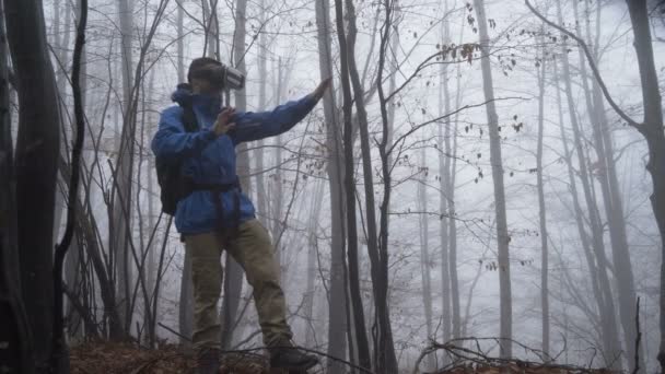 Virtual reality concept of a man in tourist clothes backpack and VR glasses in misty forest. — ストック動画