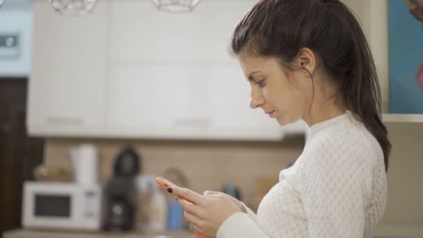 Chica morena con suéter blanco usando teléfono inteligente, mensajes de texto y lectura — Vídeo de stock