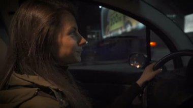 Beautiful young woman driving car at night in city traffic