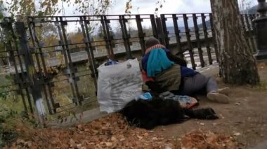 Homeless person asleep on a fence near river with bag of clothes near