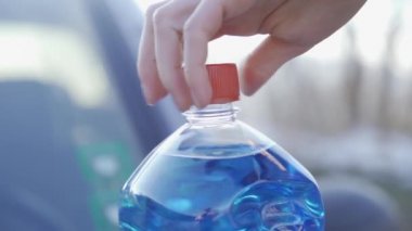 Kadın eli yavaşça silecek sıvısı şişesini açıyor.