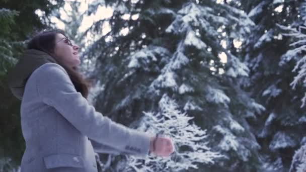 Жінка в сонцезахисних окулярах посміхається, кидаючи жменьку снігу в повітрі — стокове відео