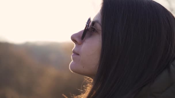 Двохвилинна жінка в сонцезахисних окулярах насолоджується сонячними променями заходу сонця — стокове відео