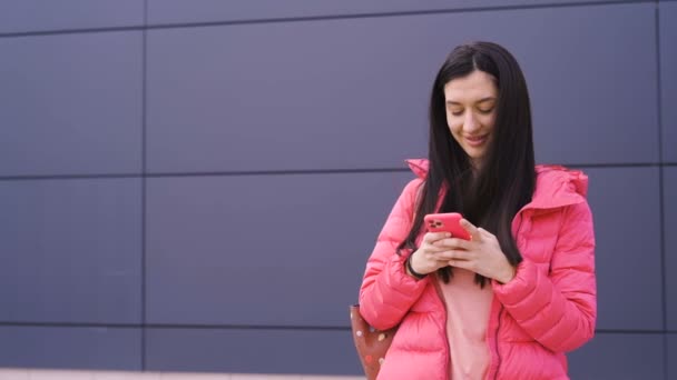 Χαριτωμένη γυναίκα σε ροζ χαμόγελα κατά τη χρήση smartphone, γραπτών μηνυμάτων με κάποιον — Αρχείο Βίντεο