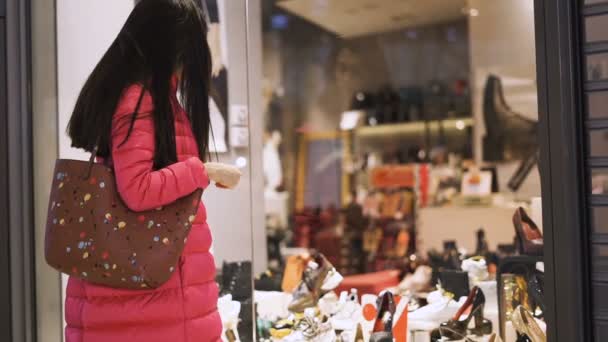 Κομψό κορίτσι βλέποντας παπούτσια στο εμπορικό κέντρο μέσα από το παράθυρο βιτρίνα — Αρχείο Βίντεο