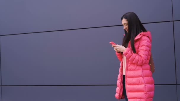 若いです美しいビジネス女性で長いピンクのジャケット笑顔と使用電話 — ストック動画