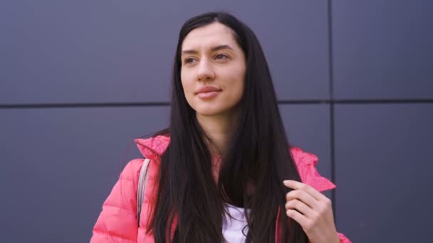 Mujer joven pensativa jugando con su pelo largo vestido con chaqueta rosa — Vídeo de stock