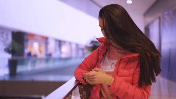 Chica de ensueño con el pelo largo mensajes de texto en el teléfono inteligente esperando en el centro comercial — Vídeo de stock