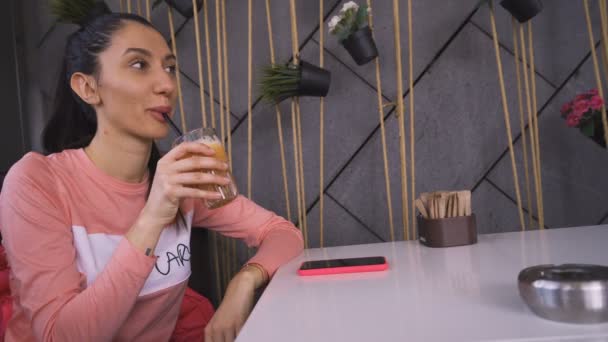 Vrouw in roze shirt neemt een slokje sinaasappelsap in cafetaria — Stockvideo