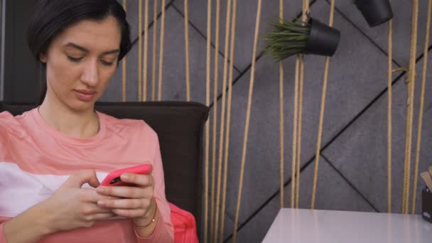 Mujer en camisa rosa mensajes de texto en el teléfono inteligente mientras espera su orden — Vídeos de Stock