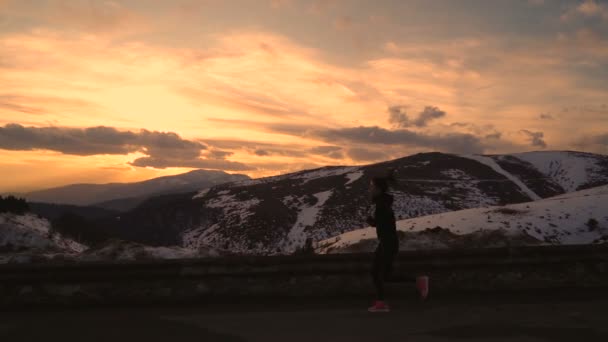 Kvinna joggare med ljusa rosa skor och svarta sportkläder sprintning i slow motion mot vacker gyllene solnedgång i snöiga berg — Stockvideo