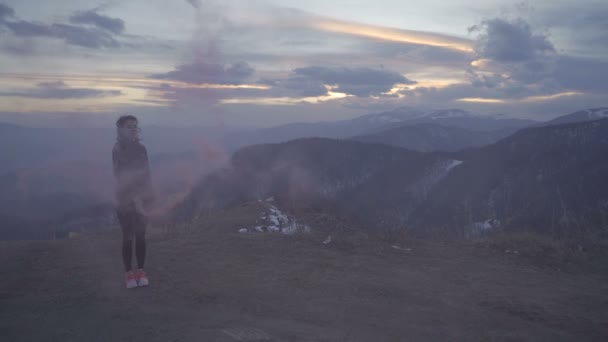 Glad fri kvinna firar seger på toppen av berget vid solnedgången med röd rök flare — Stockvideo