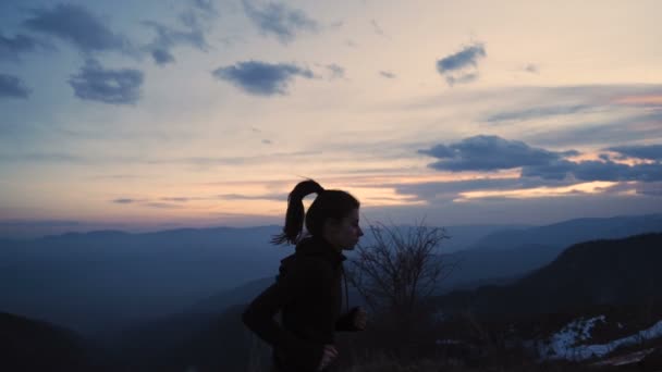 Lány lófarok integet, ahogy fut a hegyekben. Hegycsúcsok gyönyörű naplemente égbolttal — Stock videók