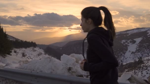 Frauenhaare wehen, als sie im Winter gegen den goldenen Sonnenuntergang auf den Gipfel des Berges rennt — Stockvideo