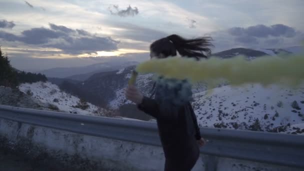 Siguiendo feliz mujer enérgica y segura con bengala de humo amarillo corriendo por el camino de asfalto en las montañas. Celebrando la victoria — Vídeos de Stock