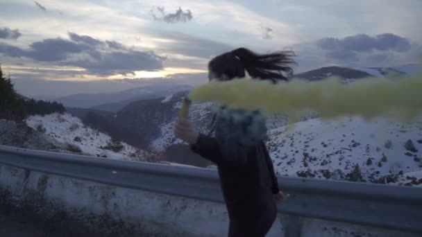 Seguindo mulher confiante energético feliz com chamas de fumaça amarela correndo na estrada de asfalto nas montanhas. Celebrando a vitória — Vídeo de Stock