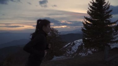 Kararlı bayan koşucu dağın tepesine ulaşmayı hedefliyor. Gün batımı gökyüzü parlak renkler ve kara bulutlar