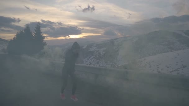 夕暮れ時に雪山の道を黄色い煙の中を走る若い女性を決定した — ストック動画