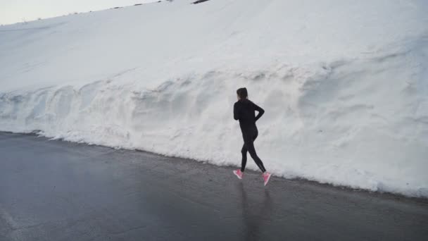 ブルガリアの山の雪の回廊で春の明るいピンクのランニングシューズとロンリージョガー — ストック動画