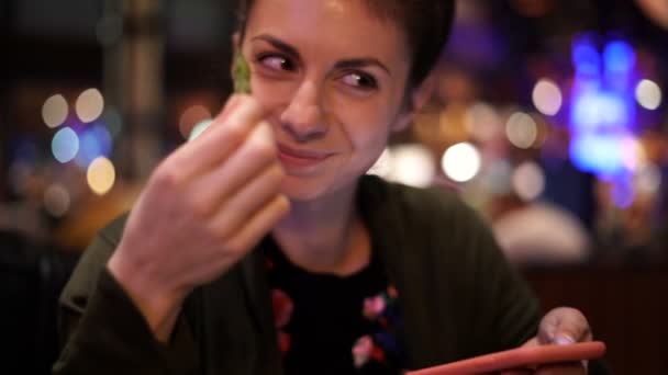 Красивая женщина ест горох, наблюдая за телефоном в ресторане, широко улыбаясь — стоковое видео