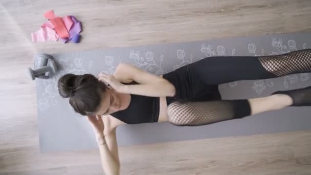 Женщина в черных штанах для йоги делает хруст на коврике для йоги — стоковое видео