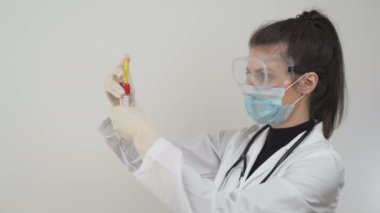 Koruyucu yüz maskesi ve gözlüklü kadın doktor ölümcül koronavirüs için kan örnekleri test ediyor.