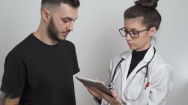 Genç bayan doktor, hastanın semptomlarını not ediyor ve adama koronavirüsün tehlikesini anlatıyor.