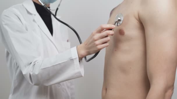 Beyaz önlüklü doktor steteskopla erkek hasta akciğerlerini inceliyor. Klinikte Coronavirus testleri — Stok video