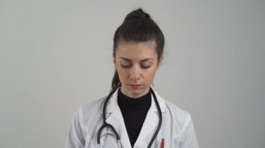 Beyaz önlüklü genç bayan doktor gülümsüyor ve kameraya poz veriyor.