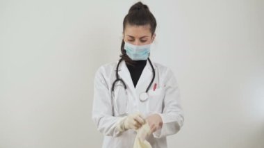 Coronavirus hastalığının önlenmesi için nasıl eldiven takılacağını gösteren genç bir kadın doktor.