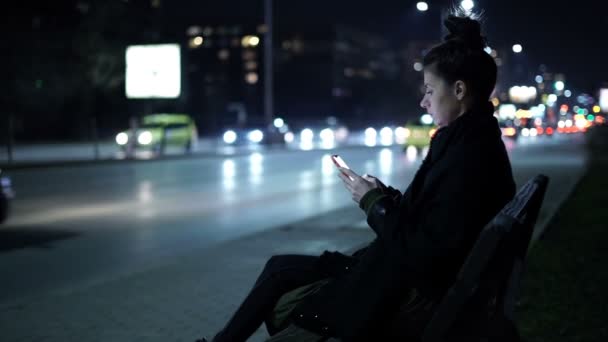 Samotna kobieta siedząca nocą na autostradzie z samochodami przejeżdżającymi obok niej — Wideo stockowe