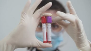 Kadın doktor elinde kanla boşta gezenleri tutuyor, kan toplama tüplerini sallıyor.