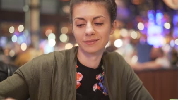 Smiling woman having dinner in restaurant. Blurred lights in the background — Stock Video