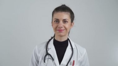 Beyaz önlüklü güzel bayan doktor gülümsüyor. Omuzlarına steteskop takmış.