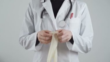 Beyaz önlüklü doktor elinde lateks eldivenle kendini koronavirüsten nasıl koruyacağını gösteriyor.