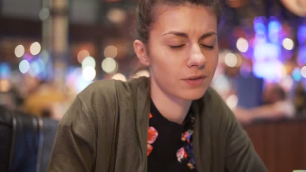 Chica emocionada tomando un bocado de comida china usando palillos. Conversar con un amigo en el restaurante — Vídeos de Stock