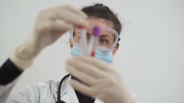 Maskeli ve koruyucu gözlüklü kadın doktor koronavirüs kan testleri üzerinde çalışıyor. COVID-19 aşı üretimi