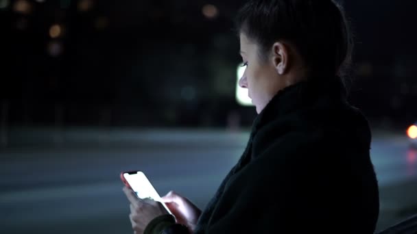 Csinos fiatal nő ül a padon egyedül az éjszakai utcában — Stock videók