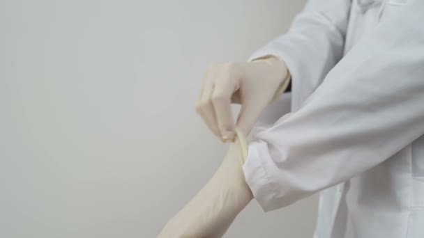 Jonge vrouwelijke arts in witte vacht demonstreert hoe beschermende handschoenen aan te brengen. COVID-19 — Stockvideo