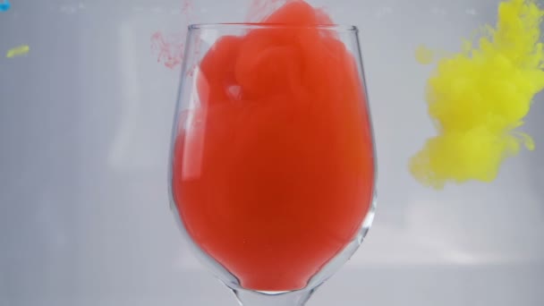 La peinture de couleur jaune, bleue et rouge tombe dans l'eau en verre au mouvement lent — Video