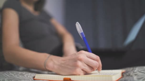 Nauwe blik van de vrouw opschrijven in boek tijdens het werken op laptop van thuis — Stockvideo