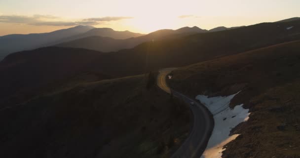 Drone follows lonely car driving on majestic winding mountain road at golden sunset — Stock Video