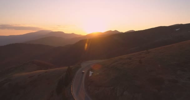 Drone siguiendo coche solitario conduciendo en carretera de montaña curva que refleja las luces de la puesta del sol — Vídeos de Stock