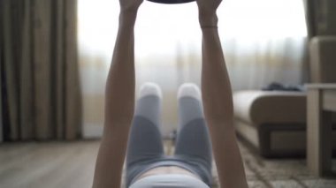 Genç ve formda bir kız evde dambıl kullanarak göğüs ve kol kası egzersizi yapıyor.