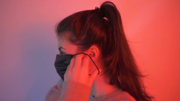 Genç kadın, koronavirüs önleme ve koruma için yüz maskesi kulaklığı takmayı gösteriyor. — Stok video