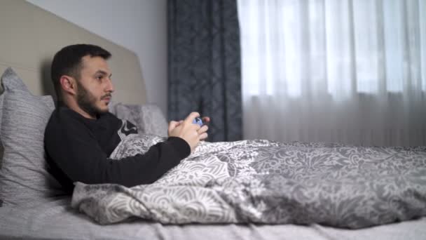 Jovem em quarentena jogando videogames na cama usando o controlador — Vídeo de Stock